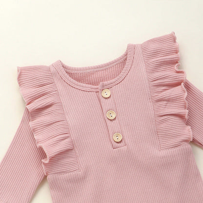 This adorable long sleeve ruffle romper features ribbed fabric with ruffled shoulders and wooden button accents, perfect for baby's cute and comfy style. A&S Collection